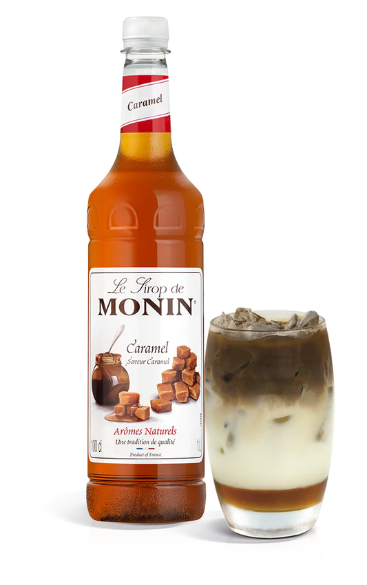 A bottle of Monin Caramel Syrup with a glass of caramel latte next to it.